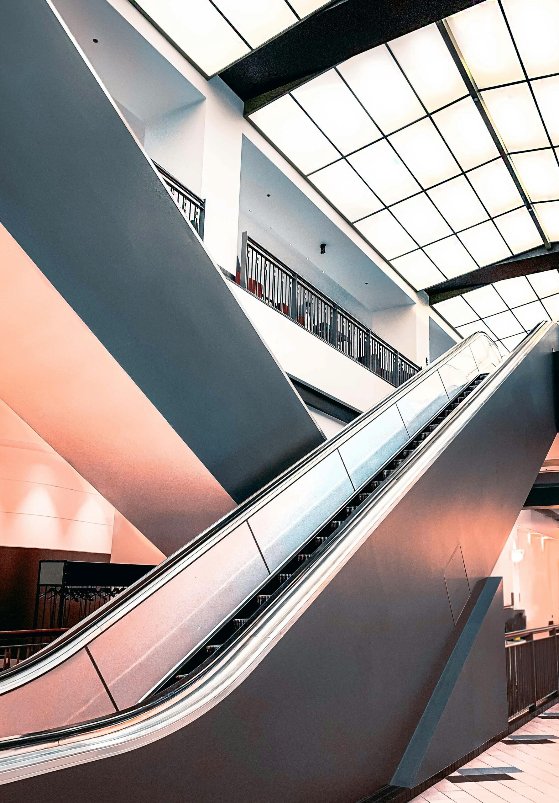 About Wide-angle view of a sleek escalator inside a modern shopping center with glass elements.